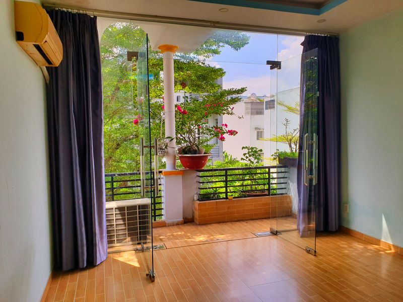 Phòng có cửa kính lớn mở ra ban công trồng cây, nhiều ánh sáng tự nhiên